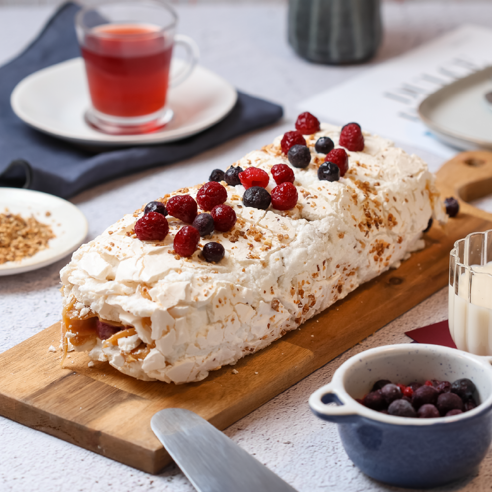 Rollo de merengue relleno con manjar y frambuesa. Incluye fruta para decorar