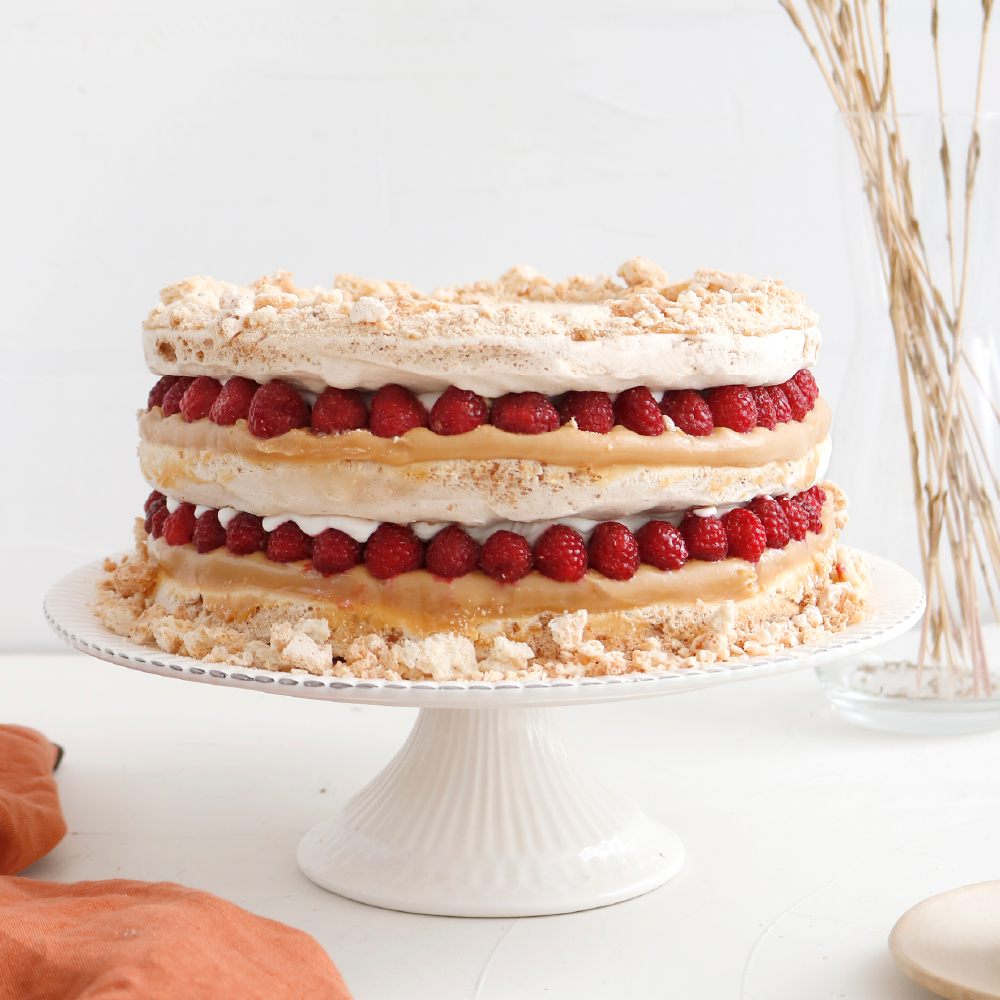 Torta de merengue con almendras, rellena de manjar, crema y frambuesas enteras