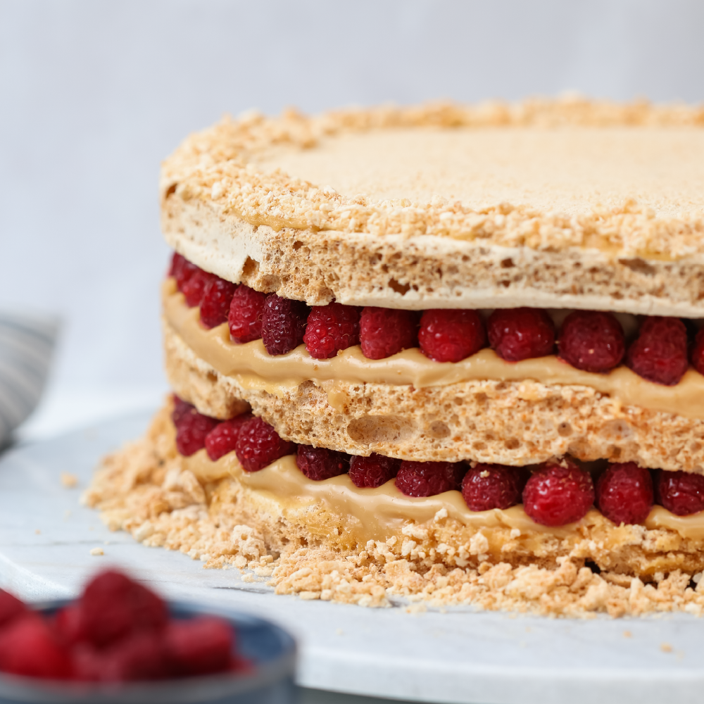 Torta de merengue con almendras, rellena de manjar, crema y frambuesas enteras